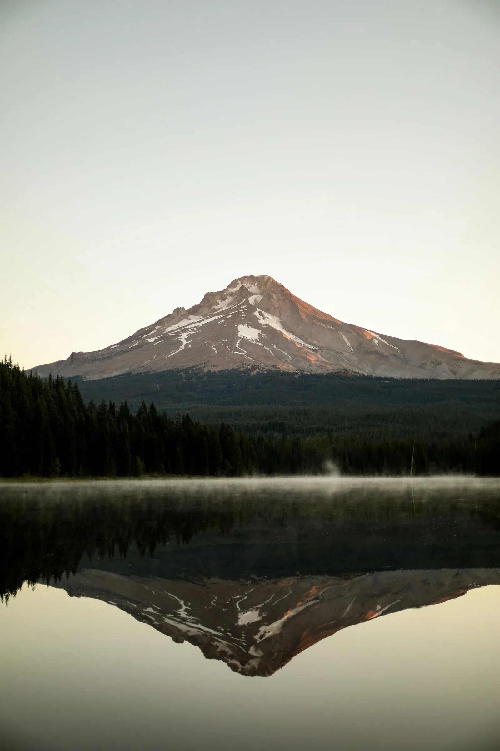 Una montaña nevada reflejada en un lago en calma, al amanecer